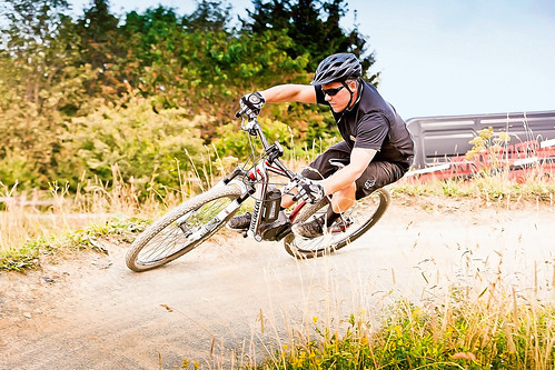 Man wearing helmet riding e-bike on a dirt track in a foothills setting.